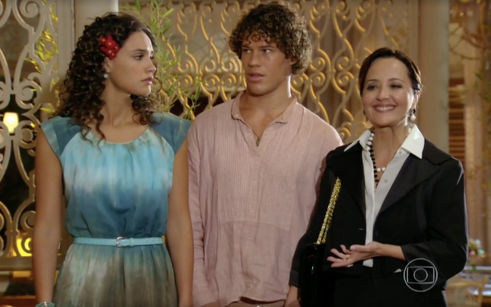 Débora Nascimento como Taís à esquerda olha para José Loreto como Candinho no centro, enquanto Claudia Netto como Guiomar fala em cena de Flor do Caribe