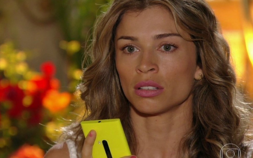 A atriz Grazi Massafera segura um celular enquanto olha para o nada caracterizada como Ester em cena de Flor do Caribe