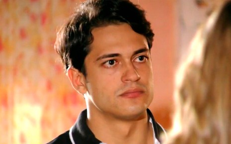 Raphael Vianna em cena de Flor do Caribe: caracterizado como Hélio, o rapaz olha sério para alguém fora do quadro