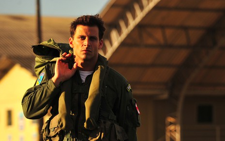 O ator Henri Castelli com uniforme militar está na frente de um hangar de aviões caracterizado como o Cassiano em cena de Flor do Caribe
