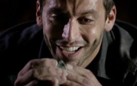 O ator Henri Castelli com um sorriso no gosto segura uma pedra preciosa esverdeada como Cassiano em Flor do Caribe