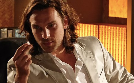 O ator Igor Rickli segura um cristal de sal com a mão direita e olha fixamente para o mineral caracterizado como o Alberto em cena de Flor de Caribe