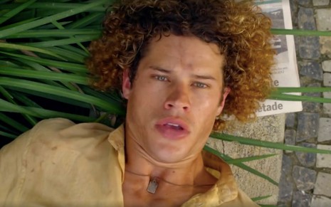 O ator José Loreto deitado em um chafariz com mato crescendo em volta caracterizado como Candinho em cena de Flor do Caribe