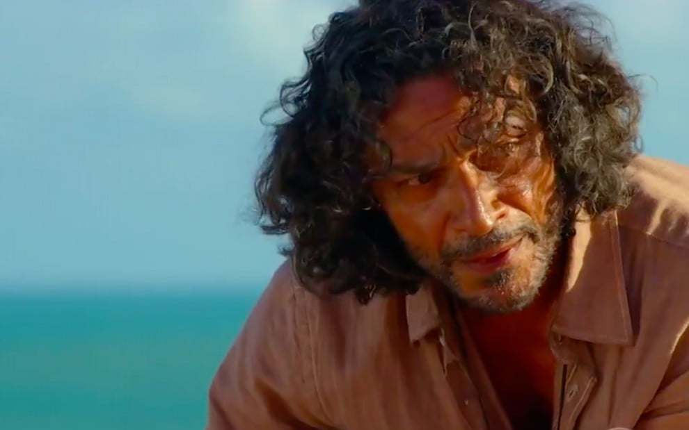 O ator Luiz Carlos Vasconcelos com o mar azul ao fundo e vento nos cabelos caracterizado como o Donato em cena de Flor do Caribe