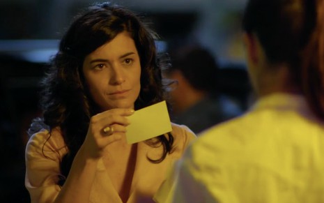 A atriz Moro Anghileri com expressão de revolta segura um cartão com a mão direita caracterizada como Cristal em cena de Flor do Caribe