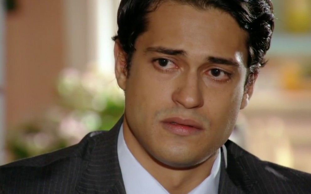 O ator Raphael Vianna caracterizado como Hélio com expressão de falsa tristeza em cena de Flor do Caribe