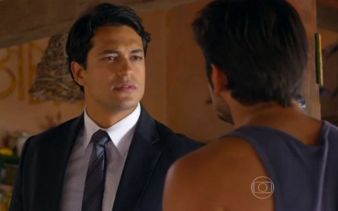 O ator Raphael Vianna, com um terno e gravata, em cena como Hélio, em Flor do Caribe