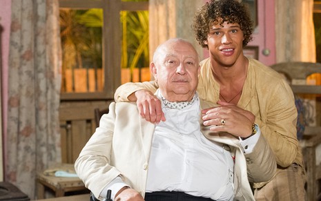 Sentado em uma cadeira de rodas, Sérgio Mamberti como Dionísio recebe um abraço de José Loreto, o Candinho, em cena de Flor do Caribe