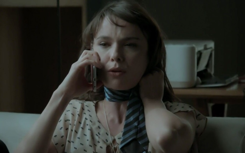 Débora Falabella em cena de A Força do Querer: personagem finge estar se sufocando com gravata e fala no telefone