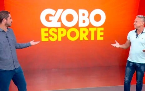 No cenário laranja do Globo Esporte, Felipe Andreoli, de camisa cinza, abre os abraços igual a Paulo Nunes ao seu lado, de camiseta branca