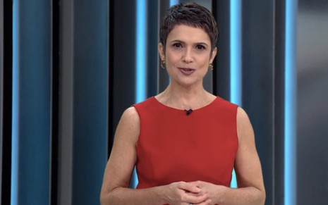 Com um vestido vermelho, Sandra Annenberg está com as mãos entrelaçadas à frente do corpo no cenário do Globo Repórter