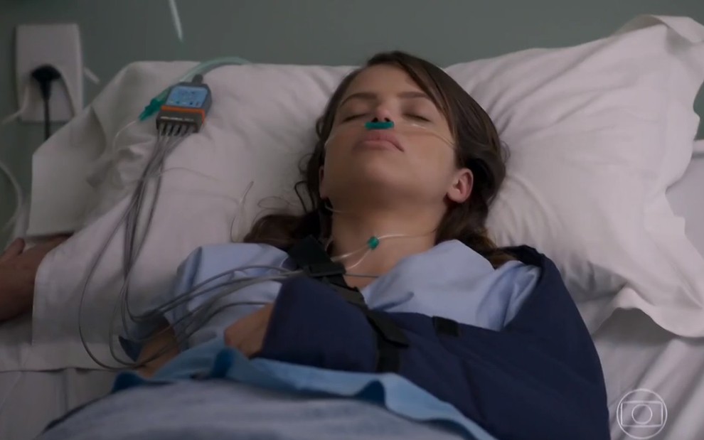 A atriz Agatha Moreira, deitada em uma cama de hospital, em cena como Camila em Haja Coração