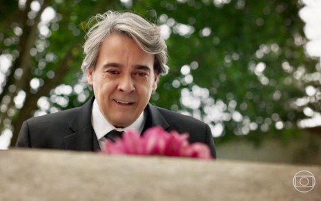 O ator Alexandre Borge faz uma expressão engraçadas ao olhar para lápide em gravação de Haja Coração, da Globo