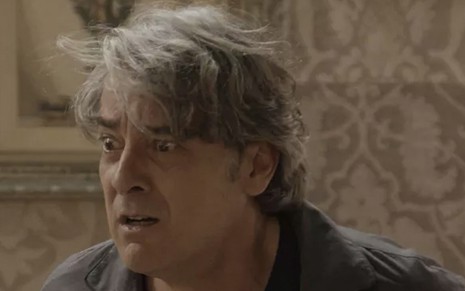 O ator Alexandre Borges com os olhos arregalados de surpresa e despenteado caracterizado como o Aparício em cena de Haja Coração