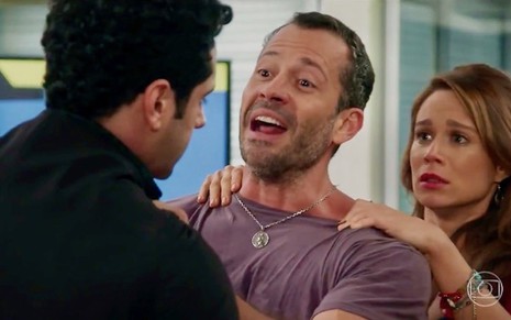 João Baldasserini (costas) é agarrado por Malvino Salvador, que tenta ser contido por Mariana Ximenes em cena  de Haja Coração