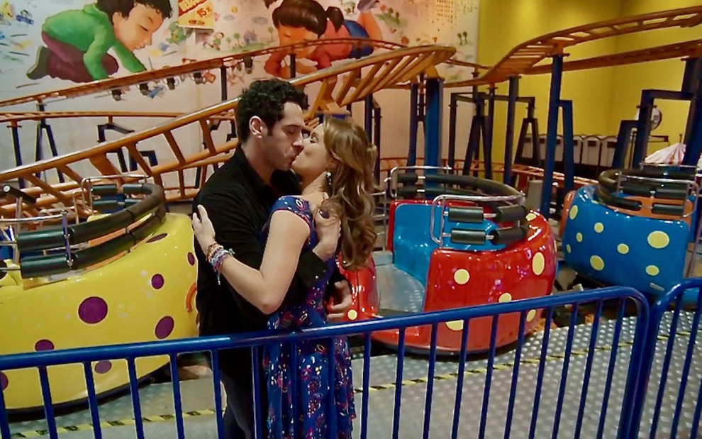 O ator João Baldasserini abraça e beija Mariana Ximenes em cenário de parque de diversões durante gravação de Haja Coração
