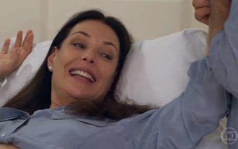A atriz Carolina Ferraz, deitada e sorrindo, em cena como Penélope, em Haja Coração