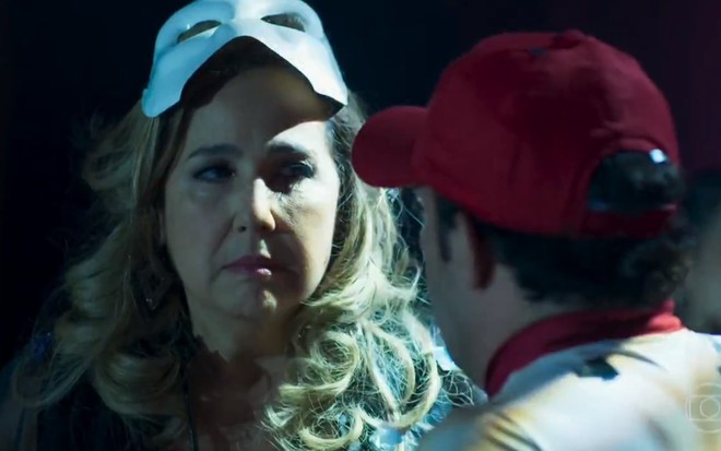 A atriz Claudia Jimenez, com uma peruca loira e uma máscara branca, em cena como Lucrécia em Haja Coração