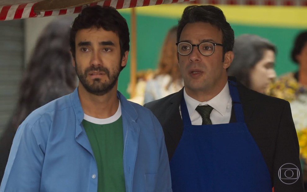 Os atores Gabriel Godoy e Marcelo Médici com avental e jaleco de feirantes em cena como Leozinho e Gigi em Haja Coração