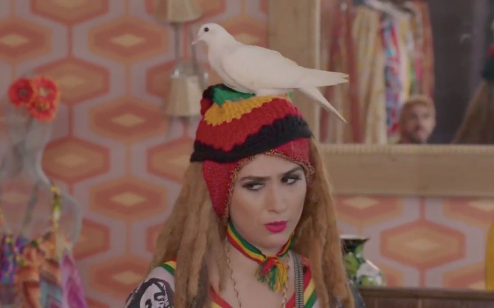 A personagem Fedora (Tatá Werneck) veste peruca rastafári e uma pomba branca está pousada em sua cabeça em cena da novela Haja Coração, da Globo