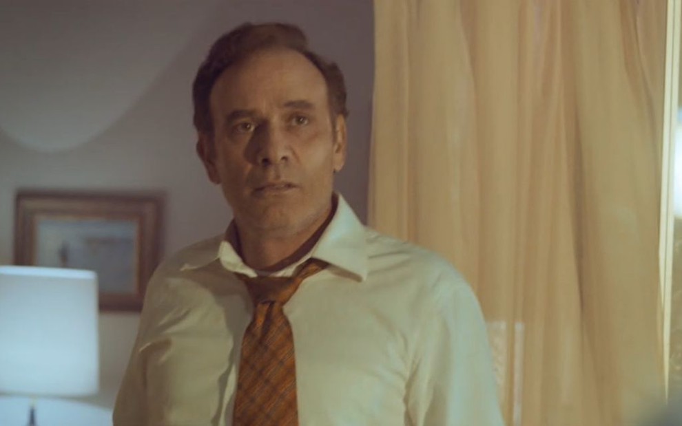 Com camisa e gravata, o ator Marco Ricca parece frustrado em cena da minissérie Hebe