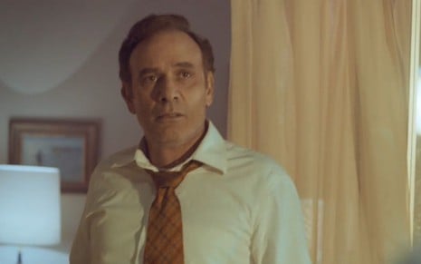 Com camisa e gravata, o ator Marco Ricca parece frustrado em cena da minissérie Hebe