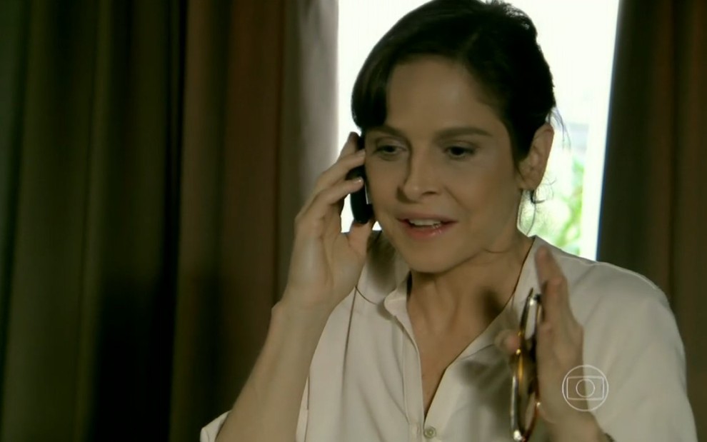 Drica Moraes grava de camisa branca com celular no ouvido e expressão de alegria como Cora de Império