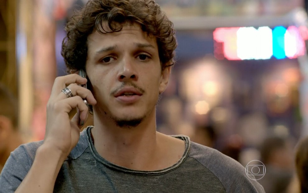 Rafael Losso grava com celular na orelha, camiseta de manga longa cinza e expressão séria como Elivaldo