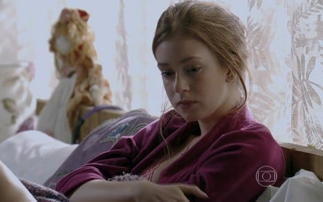Marina Ruy Barbosa grava com expressão de choro, camisa rosa, deitada na cama como Maria Isis de Império