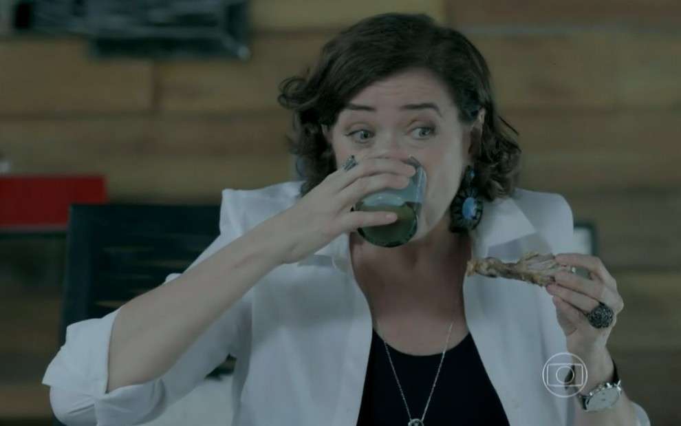 Lilia Cabral em cena com um copo de cerveja na boca e segurando um pedaço de frango nas mãos como Maria Marta de Império
