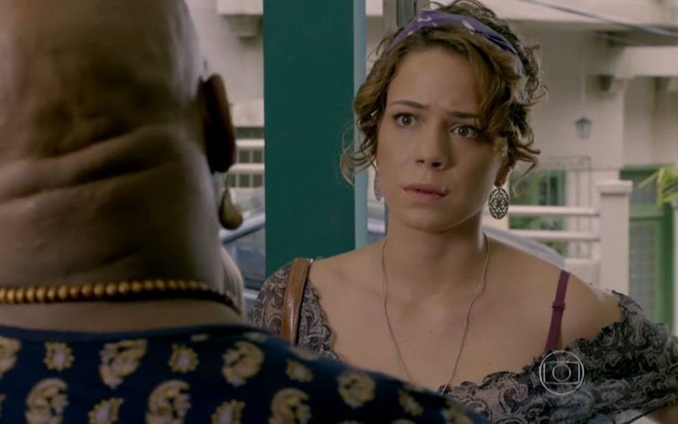 Leandra Leal grava com acessório no cabelo e blusa estampada conversando com Ailton Graça como Cristina e Xana em Império