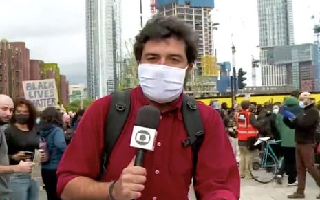 O jornalista Rodrigo Carvalho com microfone em mãos e máscaras no Jornal Hoje