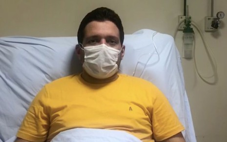 O jornalista Marcelo Magno usando uma máscara e deitado na cama de um hospital