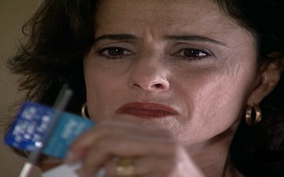 Marieta Severo com expressão de desprezo e cortando um cartão em cena como Alma de Laços de Família