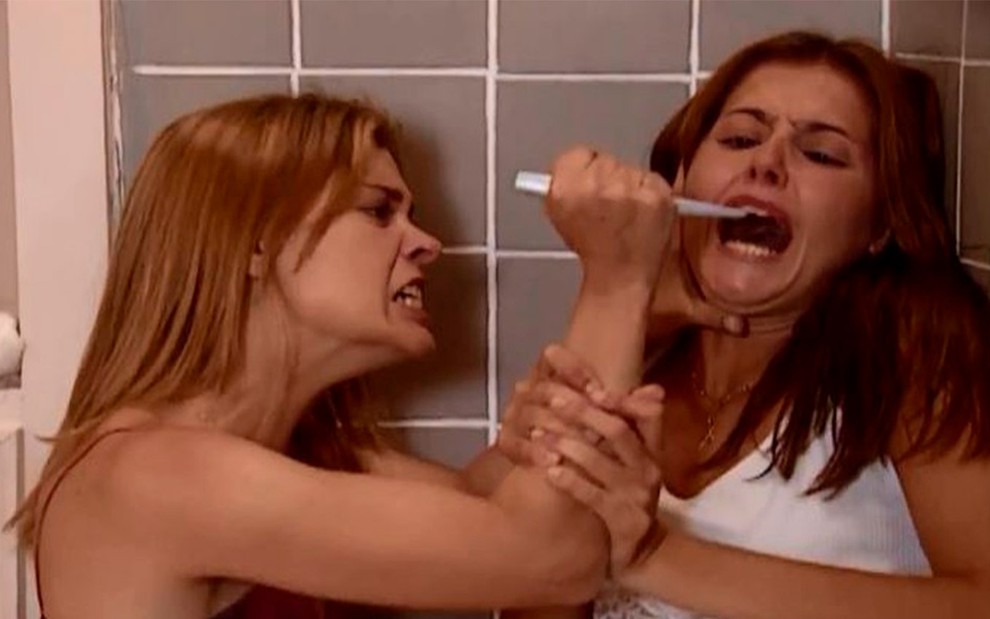 Carolina Dieckmann e Deborah Secco em cena de Laços de Família: caracterizadas como suas personagens, Carolina segura uma faca pequena no rosto da parceira de cena enquanto olha com ódio para Deborah