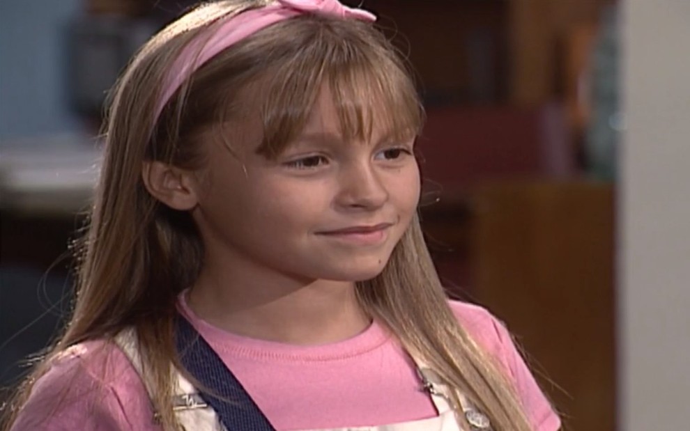 A atriz Carla Diaz, ainda criança, com uma roupa cor de rosa, em cena como Raquel em Laços de Família