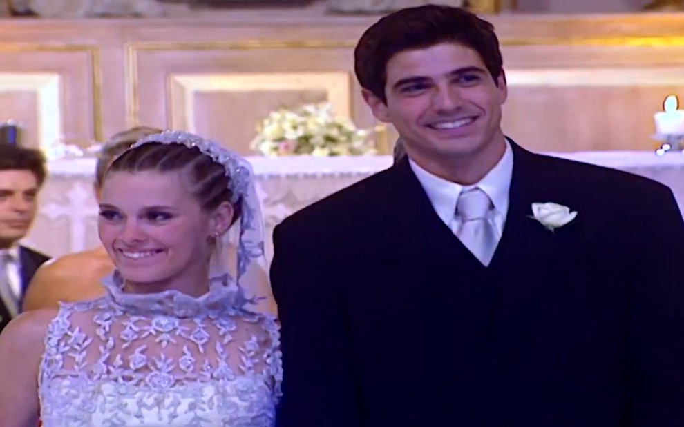 Os atores Carolina Dieckamnn e Reynaldo Gioanecchini, lado a lado, de noiva e noivo em cena como Camila e Edu em Laços de Família