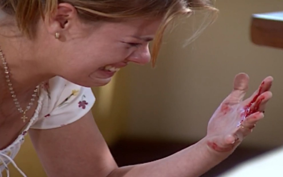 A atriz Carolina Dieckmann, chorando com a mão suja de sangue, em cena como Camila em Laços de Família