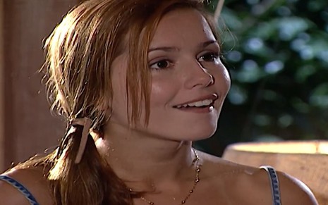 A atriz Deborah Secco, com cabelo preso de lado e sorriso no rosto, em cena como Íris em Laços de Família