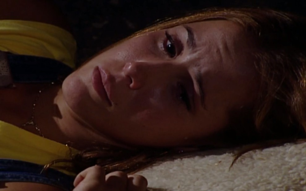 A atriz Deborah Secco dorme no chão, em cena como Íris em Laços de Família, novela que a Globo reprisa