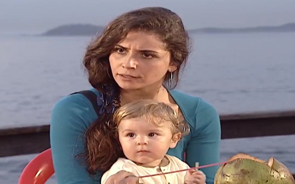 A Atriz Giovanna Antonelli, com um bebê no colo e expressão de desagrado, em cena como Capitu em Laços de Família