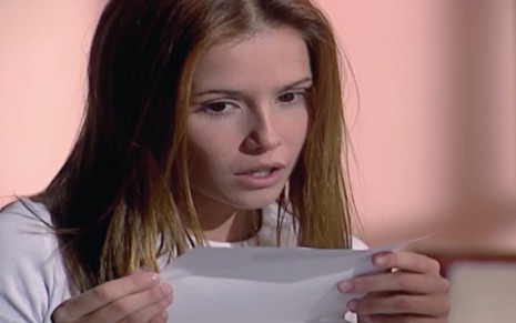 Deborah Secco em cena de Laços de Família: personagem está caracterizada como Íris e olha com curiosidade para papel