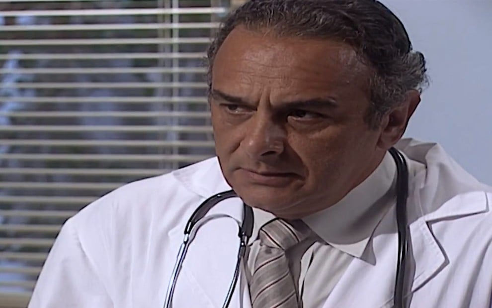 O ator Luiz Baccelli, vestido de médico e com expressão séria, em cena como César em Laços de Família