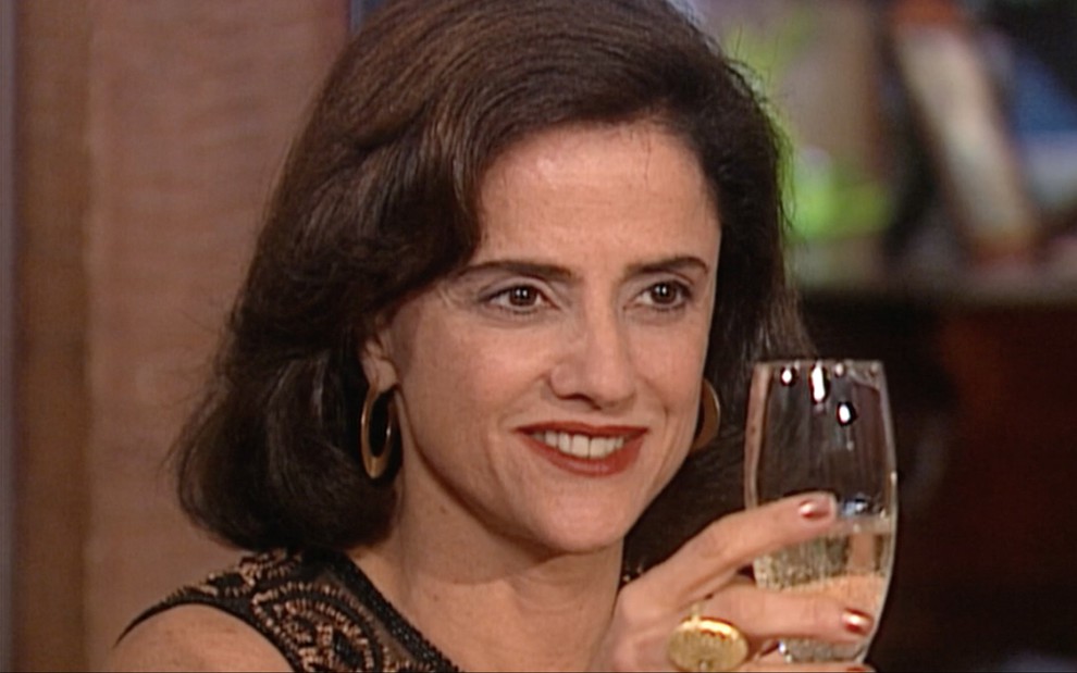 A atriz Marieta Severo levanta uma taça de champanhe como Alma em cena de Laços de Família