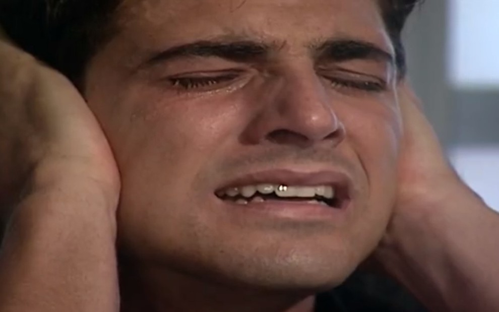 O ator Reynaldo Gianecchini, de olhos fechados, chorando com expressão de sofrimento, em cena como Edu em Laços de Família