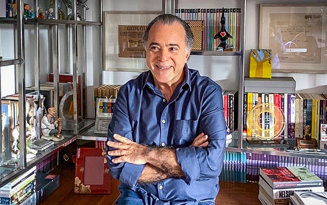 O ator Tony Ramos, de braços cruzados, posa em seu escritório com vários livros ao fundo 