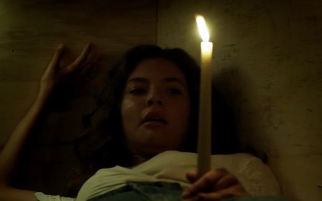 A atriz Alanis Guillen, dentro de um caixão, segura uma vela, caracterizada como a Rita em cena de Malhação: Toda Forma de Amar