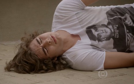 Rafael Vitti grava caído no chão com expressão de dor com camiseta branca estampada como Pedro