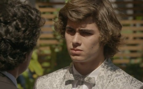 Rafael Vitti grava com terno prateado, cabelo grande e expressão séria como Pedro de Malhação Sonhos