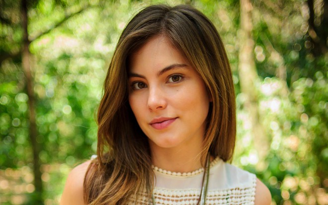 Bruna Hamú em foto de divulgação de Malhação Sonhos: atriz olha para a câmera, usa os cabelos longos de lado, regata branca e colar